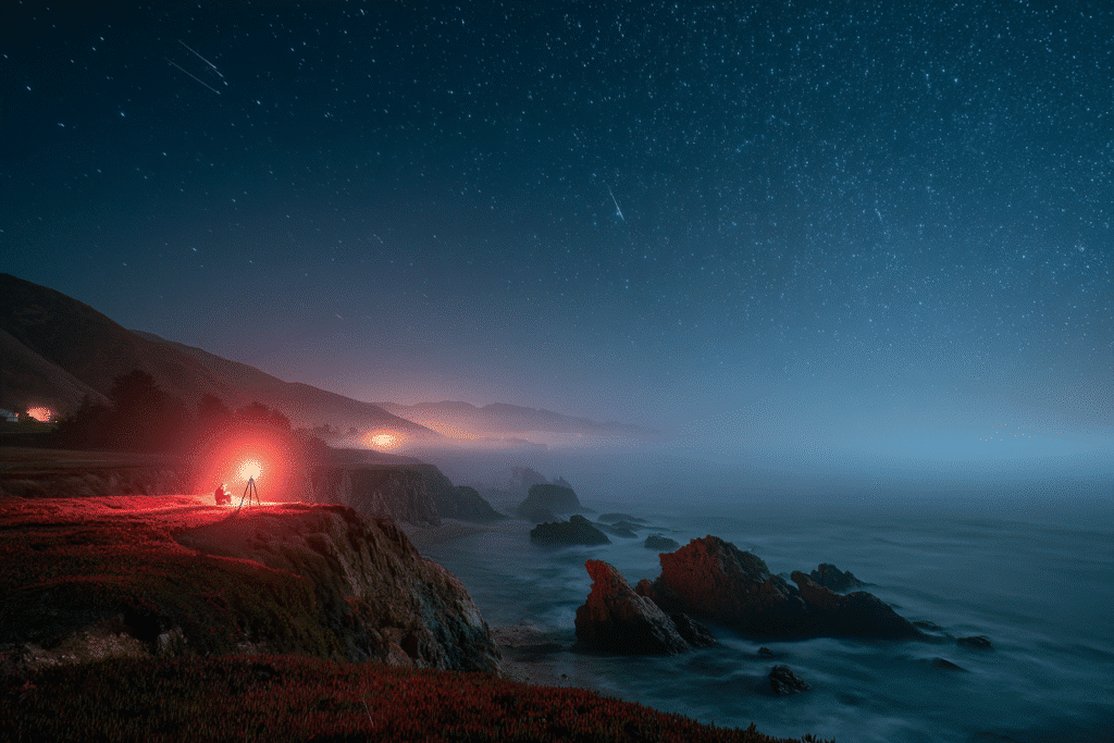 multiple taurids streaks arcing above ocean mist, red headlamp glow near a tripod camera